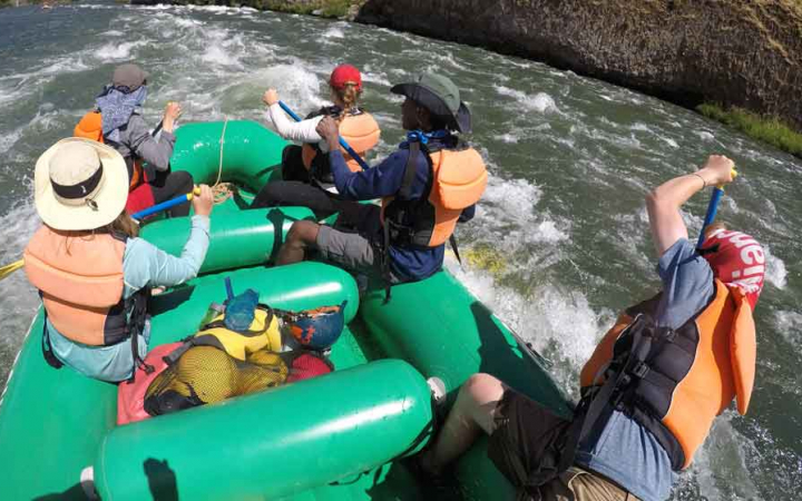 a group of adults navigate whitewater in a raft on an outward bound trip